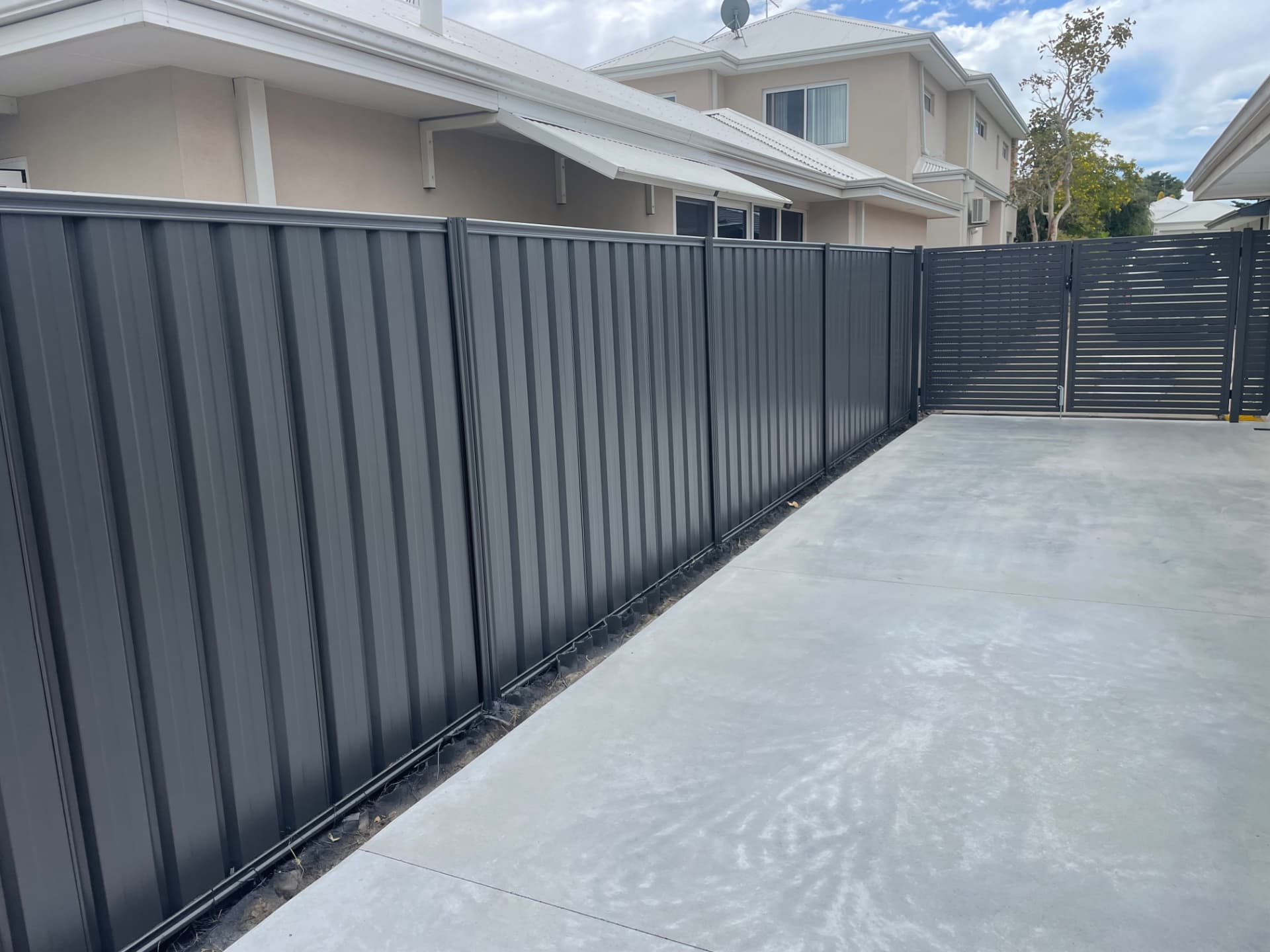 Charcoal painted corrugated fence and matching slat gate beside a concrete drive
